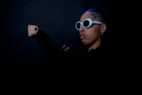 a woman with dreadlocks and sunglasses posing in front of a dark background